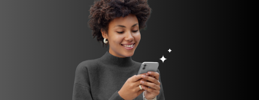 Frau schaut lächelnd auf ihr Smartphone vor schwarzem Hintergrund.