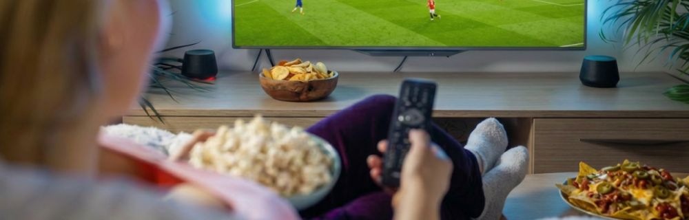 Person schaut ein Fußballspiel im Fernsehen und genießt dabei Snacks auf dem Sofa.
