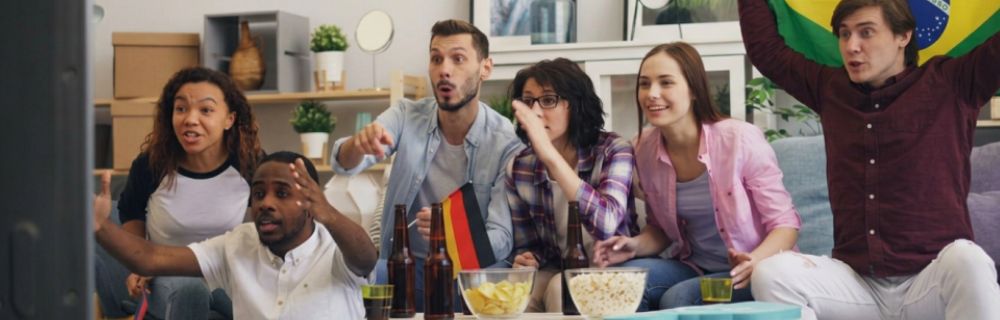 Eine Gruppe von Fußballfans verfolgt gespannt ein Spiel und jubelt vor dem Fernseher.