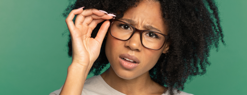 Frau mit skeptischem Gesichtsausdruck rückt ihre Brille gerade.