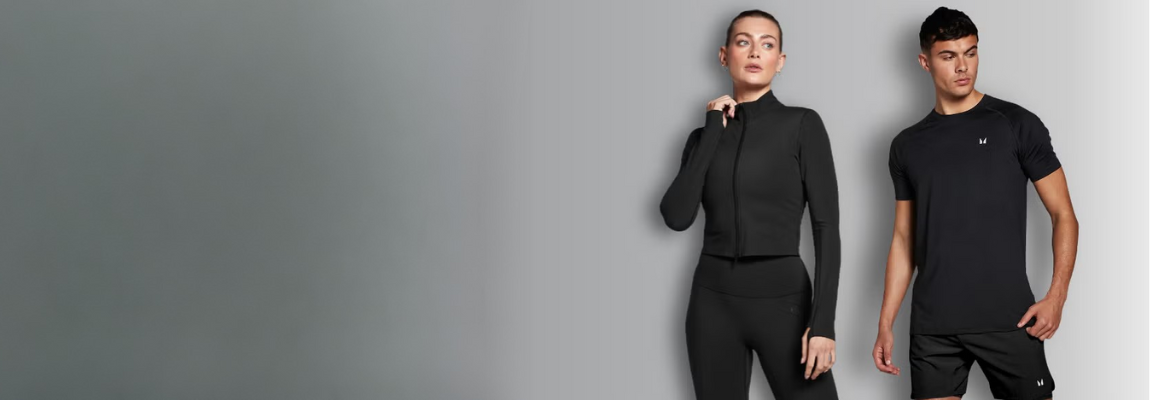 Frau und Mann tragen schwarze Trainingskleidung und stehen vor einem grauen Hintergrund.